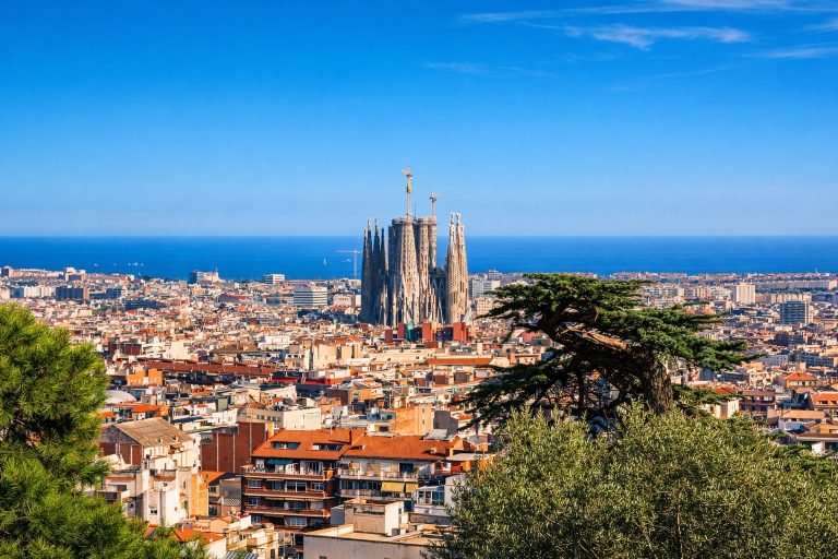 Panoramic view of Barcelona with the Sagrada Família rising above the city rooftops on a bright sunny afternoon under clear blue skies