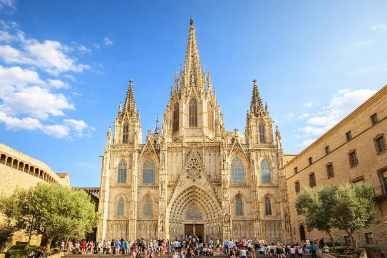 Barcelona Cathedral (La Seu) in the Gothic Quarter, viewed in landscape format on a sunny afternoon with clear blue skies and people gathered on the steps.