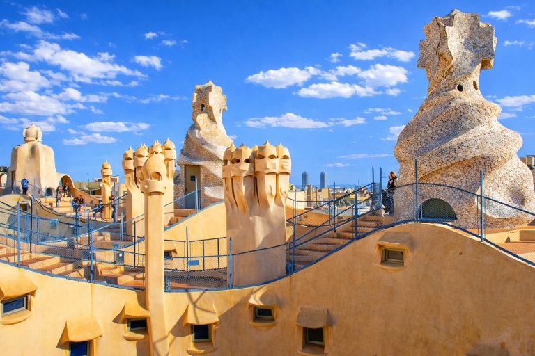 Rooftop chimneys of Casa Milà (La Pedrera) in Barcelona under a bright blue sky, showcasing Antoni Gaudí’s sculptural stone forms on a sunny afternoon.