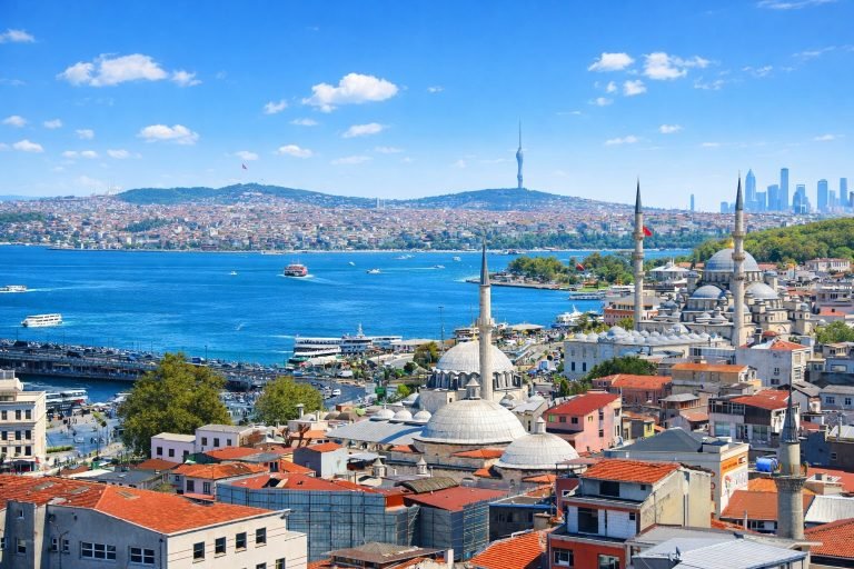 Bright, sunlit view of Istanbul with vivid blue skies, sharp city details, mosques and minarets in the foreground, and the Bosphorus sparkling in the distance.