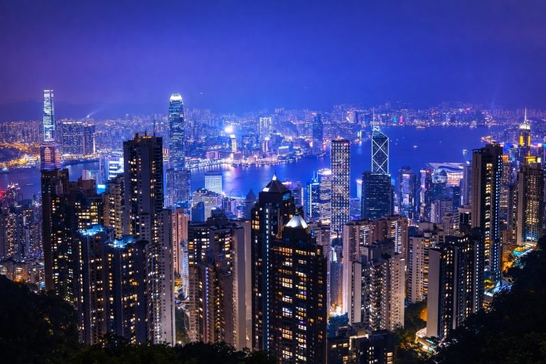 Nighttime view of Hong Kong’s illuminated skyline and Victoria Harbour, with sharp, colorful skyscrapers glowing under a clear evening sky.