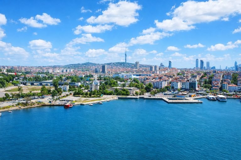 Panoramic aerial view of Istanbul on a sunny afternoon, with bright blue water in the Golden Horn, a clear blue sky, and the city skyline stretching into the distance.