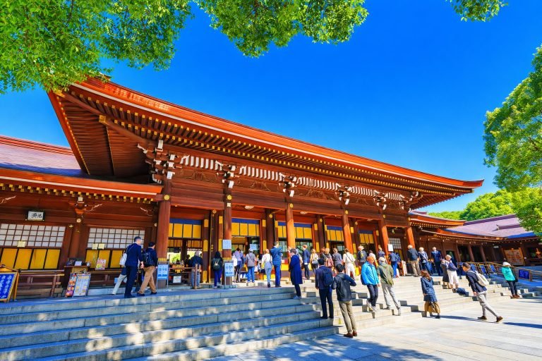Visitors walking up the steps of Meiji Shrine in Tokyo on a sunny day with blue skies and lush green trees. Caption Description