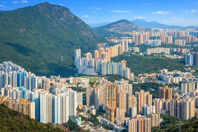Things to do in Hong Kong - Bright, crisp aerial view of Hong Kong high-rise apartment towers nestled between lush green mountains on a clear sunny day with blue skies.