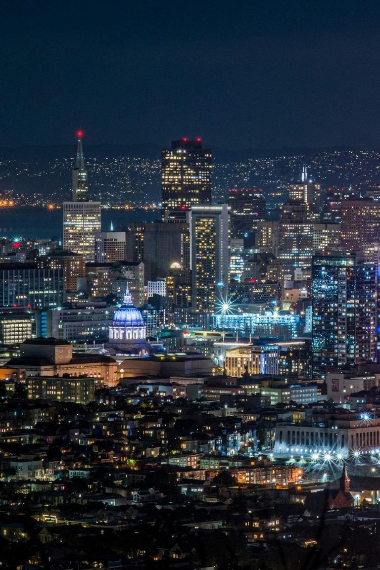San Francisco skyline at night with illuminated downtown buildings and City Hall under a dark sky