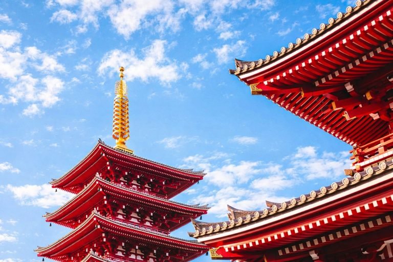 Five-story pagoda at Senso-ji Temple in Tokyo under a bright blue sky with vivid red architecture and traditional roof details.