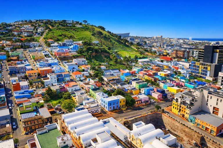 Colorful houses of Bo-Kaap in Cape Town with Table Mountain foothills and city skyline under bright blue skies
