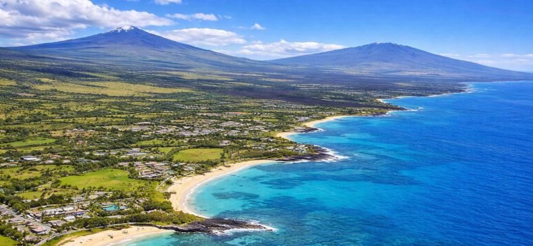 Aerial view of Hawaii’s Big Island with Mauna Kea and Mauna Loa rising inland, black lava fields, green plains, and turquoise ocean along the Kona coastline on a sunny afternoon