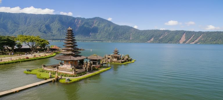 Ulun Danu Beratan Temple in Bali, set on Lake Beratan with traditional pagoda-style shrines, calm water, and green mountains under a clear blue sky.