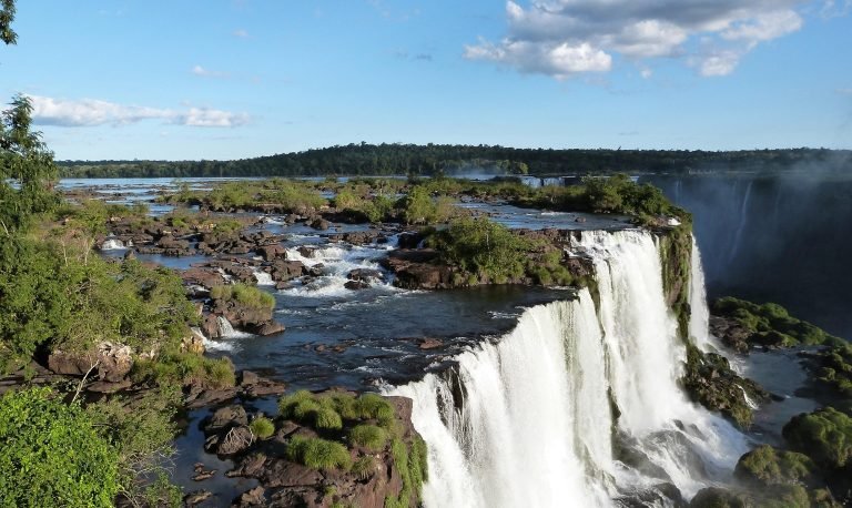 Panoramic view of Iguazu Falls in Brazil with multiple waterfalls cascading over rocky cliffs surrounded by lush greenery