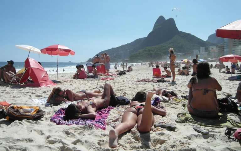 Travelers relaxing on a crowded Rio beach with Dois Irmãos mountain in the background during a things to do in Rio de Janeiro itinerary