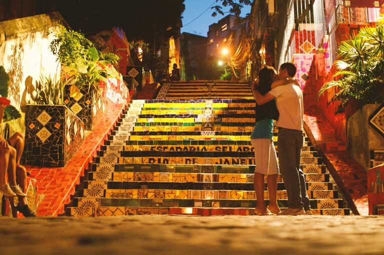 Couple standing on colorful Selarón Steps at night in Rio de Janeiro with mosaic tiles and warm lighting