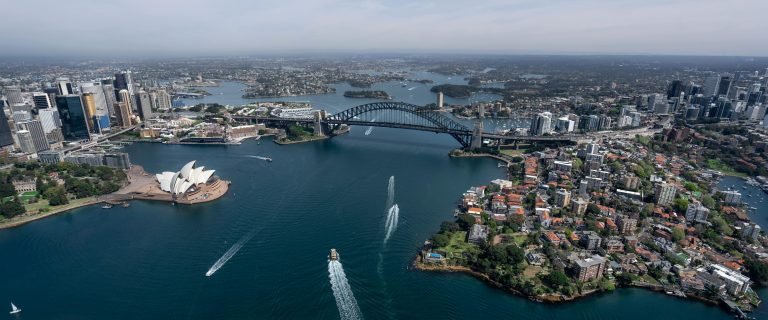 Aerial view of the Sydney Harbour Bridge spanning Sydney Harbour with boats and the city skyline in the background.