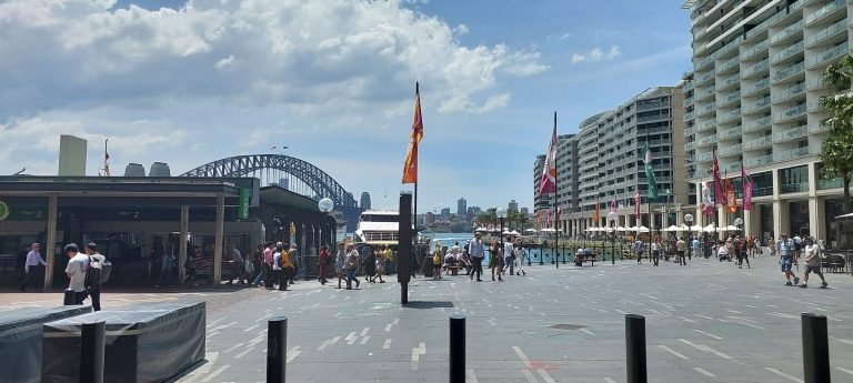 Crowds walking along Circular Quay in Sydney with the Harbour Bridge in the background on a sunny day.