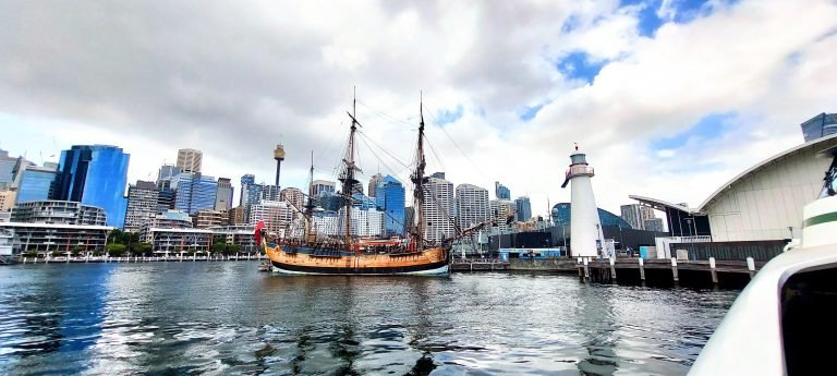Historic tall ship at Darling Harbour with Sydney CBD skyline and lighthouse in the background.