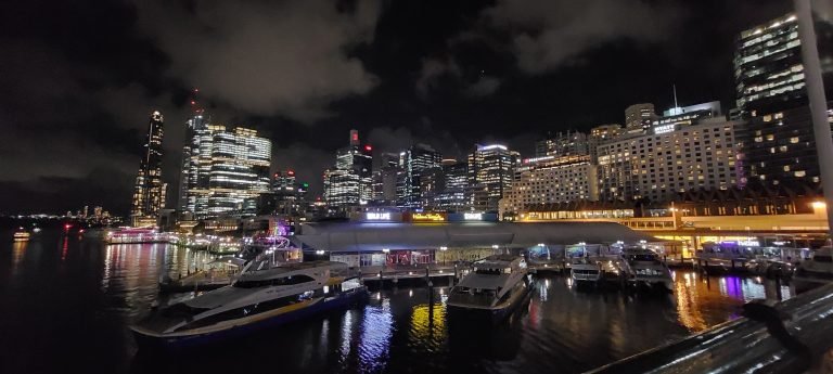 Sydney skyline at night over Darling Harbour with boats docked and city lights reflecting on the water.