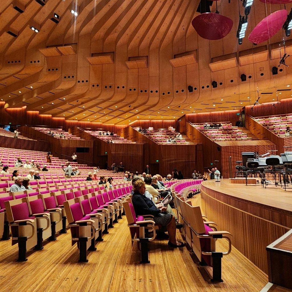 Sydney Opera House tours: Interior of the Sydney Opera House concert hall with rows of pink seats and a stage setup for an orchestra performance.