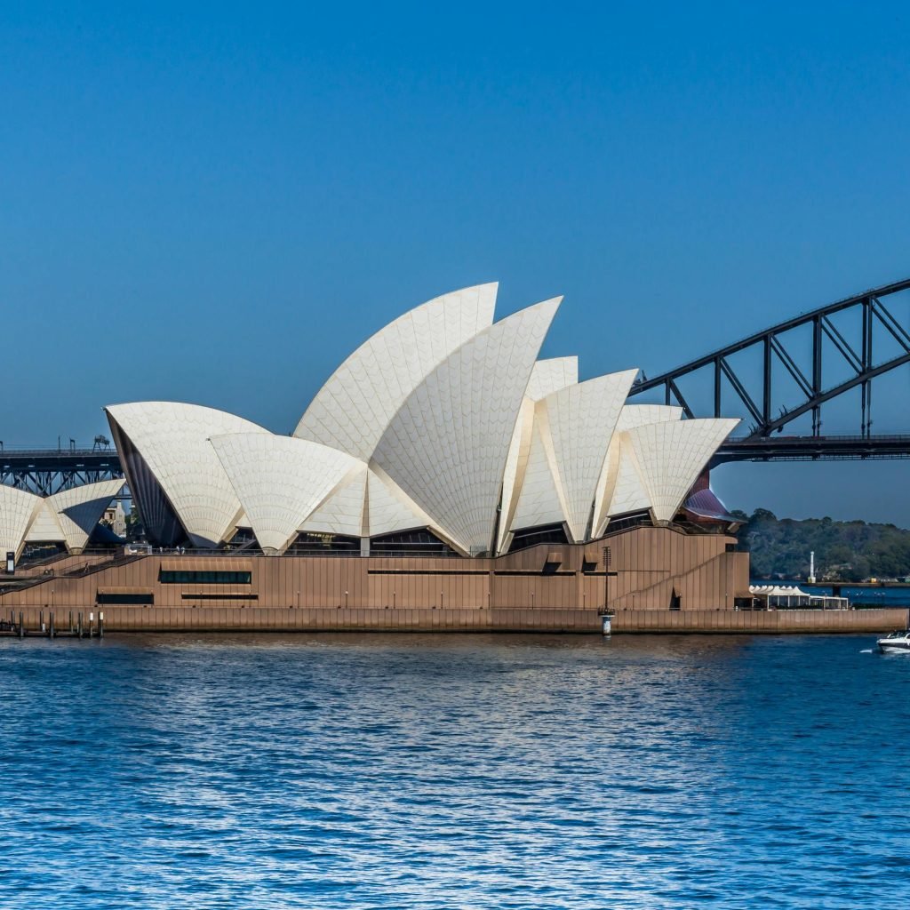 Sydney Opera House with the Harbour Bridge in the background on a bright clear day, viewed from across Sydney Harbour.