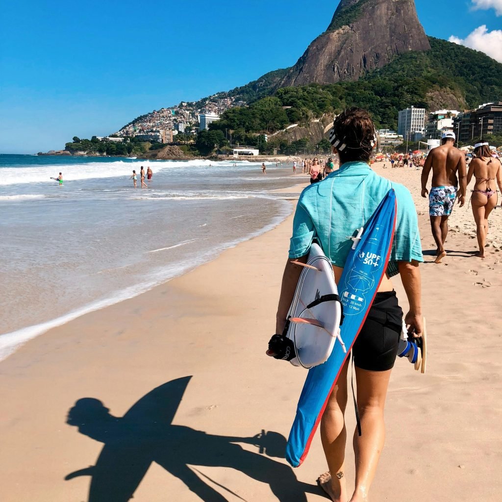Surfer walking along São Conrado beach in Rio de Janeiro with Dois Irmãos mountains in the background