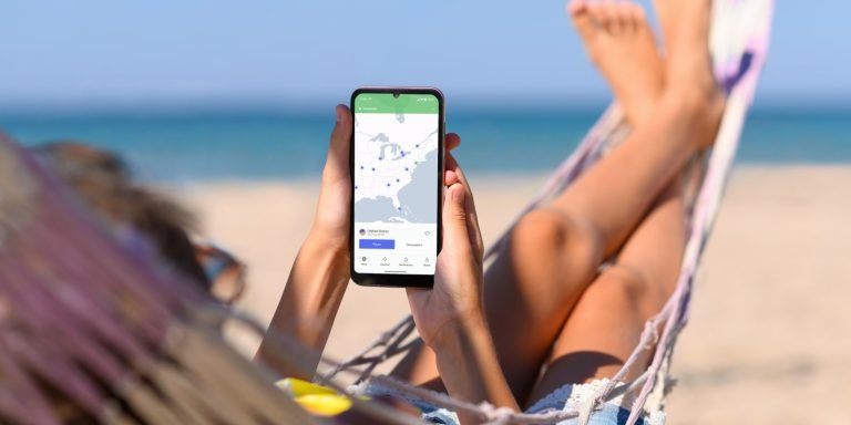 Traveler relaxing in a hammock on the beach while holding a smartphone showing a map app.