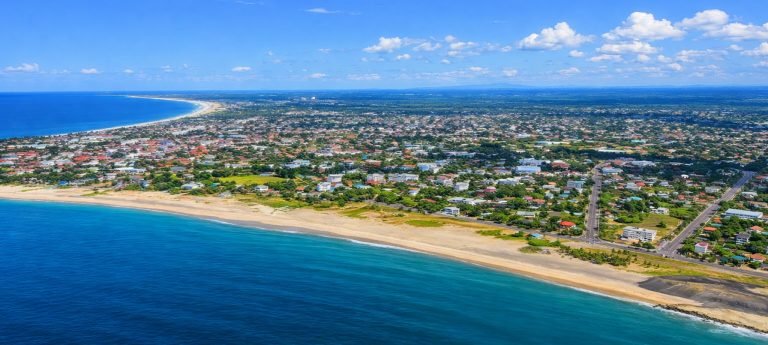 Aerial view of Toamasina (Tamatave), Madagascar, showing the long sandy coastline and turquoise Indian Ocean under bright blue skies.