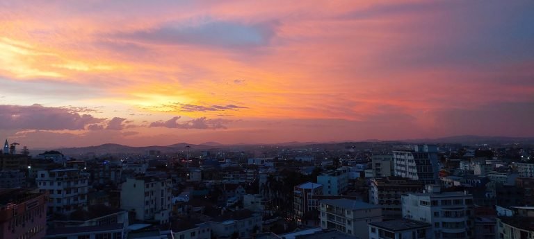 Sunset over Antananarivo with city buildings silhouetted beneath a pink and orange evening sky