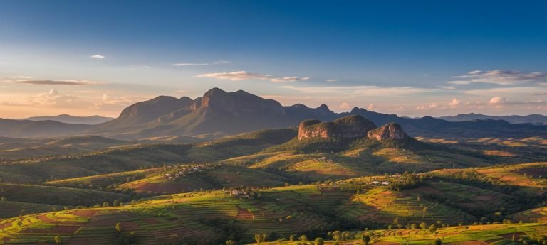 Golden-hour view over Madagascar’s Central Highlands with patchwork rice fields and distant mountains under a blue sky