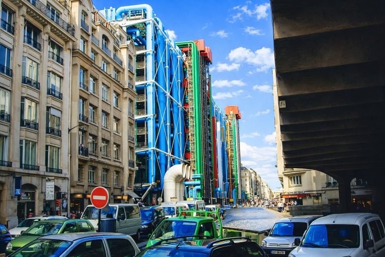 Centre Pompidou exterior with colorful exposed pipes along a Paris street on a bright sunny afternoon under clear blue skies.