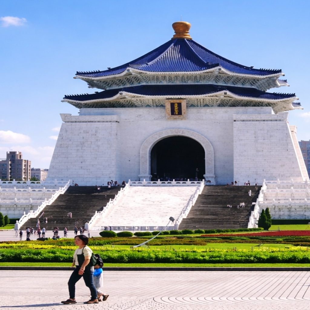 Chiang Kai-shek Memorial Hall in Taipei on a bright sunny day, with blue roof, white marble steps, gardens, and visitors in Liberty Square.