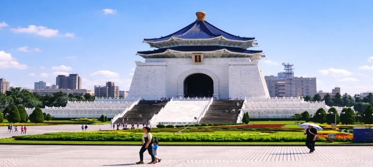 Chiang Kai-shek Memorial Hall in Taipei on a bright sunny day, with blue roof, white marble steps, gardens, and visitors in Liberty Square.