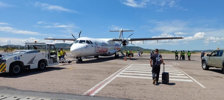 Passengers walking across the runway toward a Tsaradia turboprop plane at a Madagascar airport under a bright blue sky.