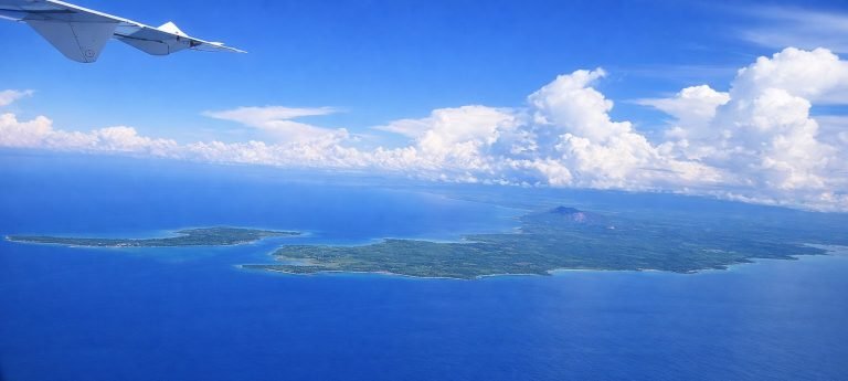 Aerial view of Madagascar’s coastline from an airplane window, showing lush green land surrounded by deep blue ocean.