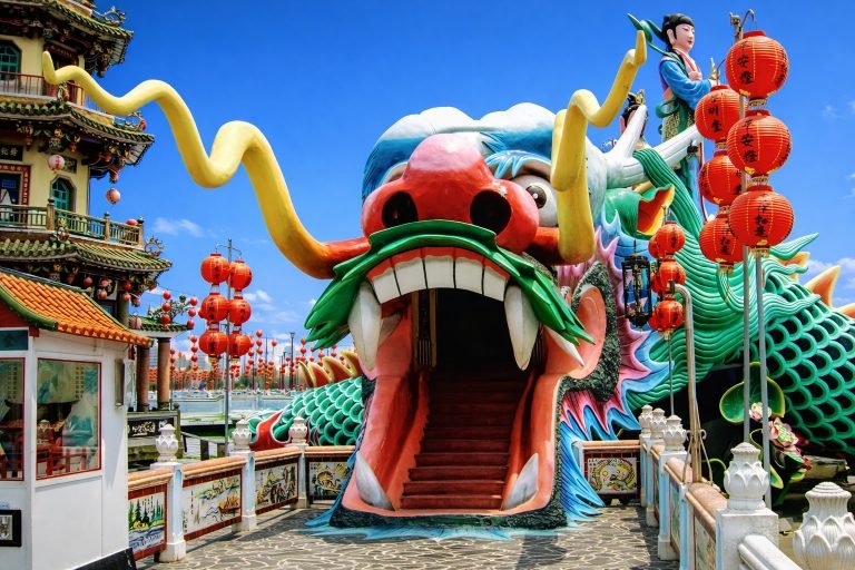 The Dragon and Tiger Pagodas entrance at Lotus Pond in Kaohsiung, Taiwan, with a colorful dragon mouth tunnel, red lanterns, and bright blue sky.