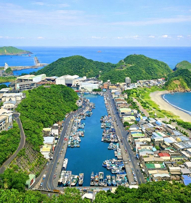 Aerial view of a fishing harbor and coastal village surrounded by green hills and blue ocean in Taiwan