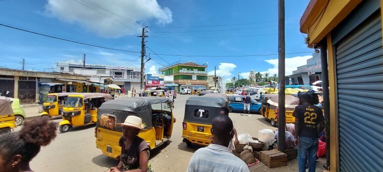 Street scene in Hell-Ville, Nosy Be, with yellow tuk-tuks, market stalls, and daily local life under a bright blue sky