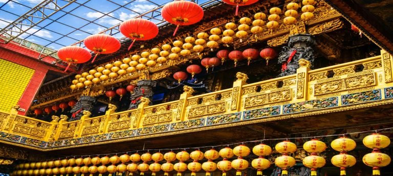 Kenting Taiwan: Ornate Taiwanese temple balcony decorated with rows of red and gold lanterns and intricate gold carvings under a bright blue sky.