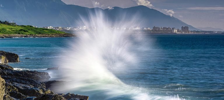 Taroko Gorge, Hualien: Powerful ocean waves crashing against rocky coastline with mountains and Hualien city in the background, Taiwan