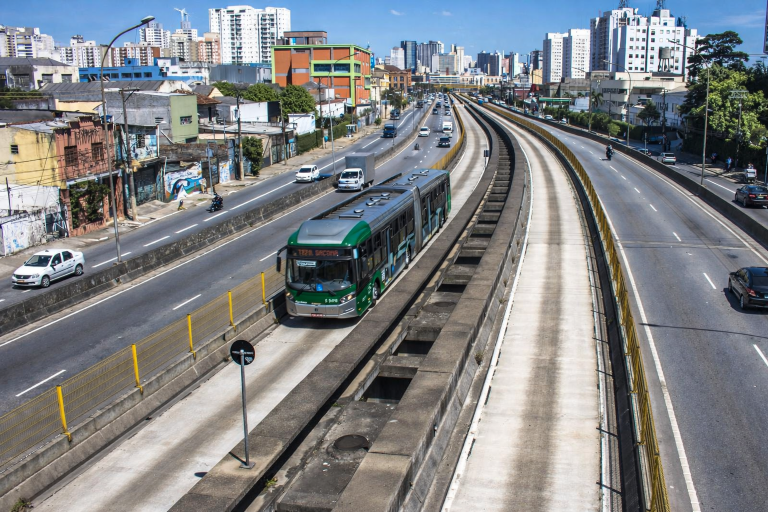 Dedicated bus corridor in São Paulo with an articulated city bus and surrounding traffic, showing how people move around the city.