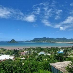 Panoramic sea view in northern Madagascar showing a coastal village, turquoise bay, and green hills under a bright blue sky.