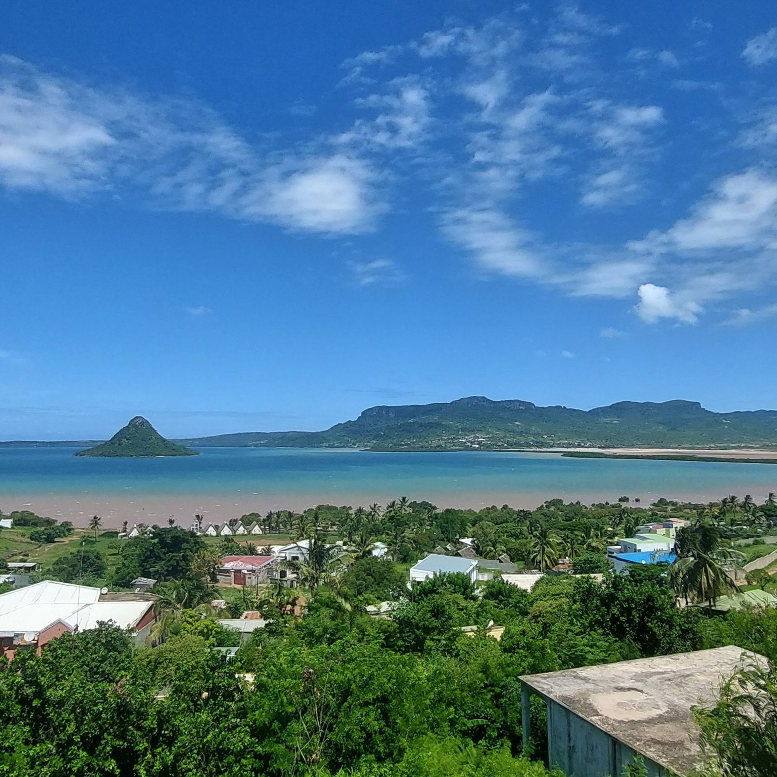 Panoramic sea view in northern Madagascar showing a coastal village, turquoise bay, and green hills under a bright blue sky.