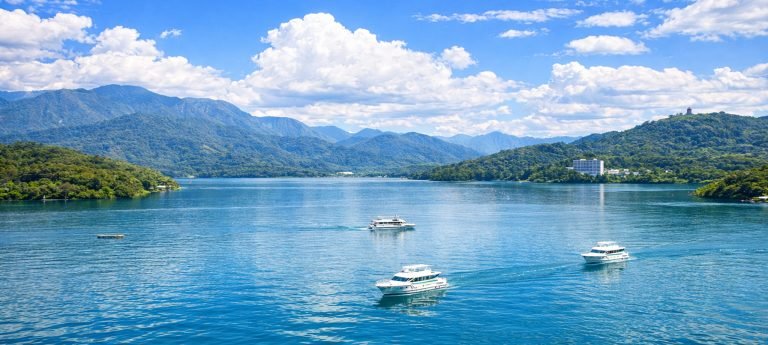 Sun Moon Lake on a sunny day with boats on the water, lush green mountains, and bright blue skies in Taiwan.