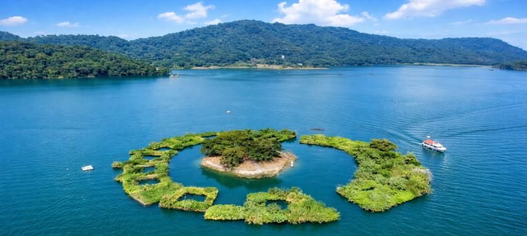 Aerial view of Sun Moon Lake with small green island, blue water, and surrounding forested mountains in Taiwan.