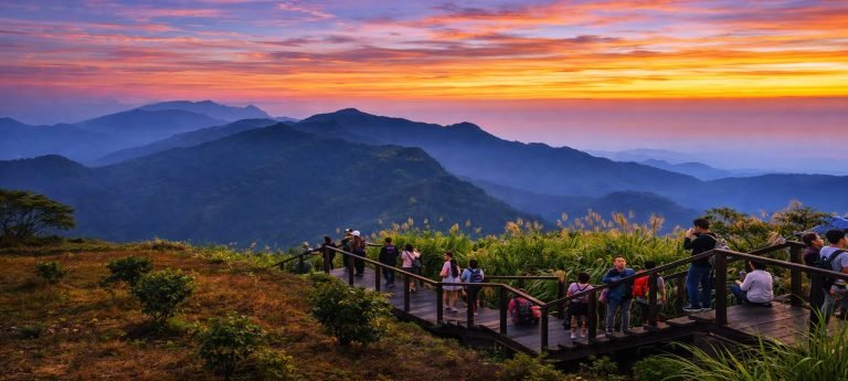 Visitors watching sunrise from a wooden viewing platform in Alishan with layered mountain peaks and colorful dawn sky
