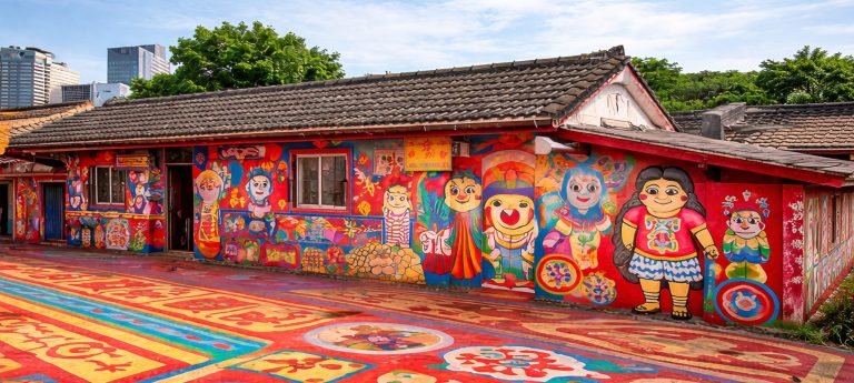 Rainbow Village in Taichung, Taiwan with colorful hand-painted murals covering the walls and ground, featuring cartoon figures and vibrant patterns under a blue sky