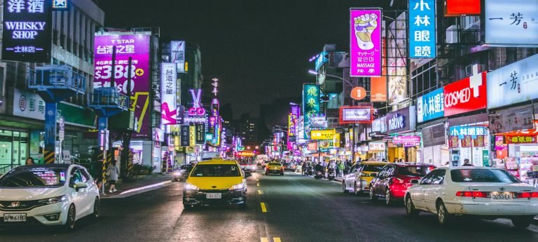 Neon-lit street in Taipei at night with bright signs, shops, taxis, and traffic in a busy downtown district.