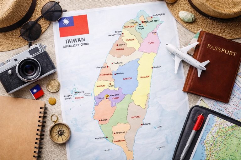 Taiwan travel planning flat lay with a colorful map of Taiwan surrounded by a camera, sunglasses, passport, compass, notebook, and a small airplane.