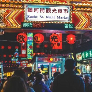 Things to do in Taiwan: Crowds walking under the illuminated entrance sign for Raohe Street Night Market in Taipei, surrounded by glowing lanterns and neon lights at night.