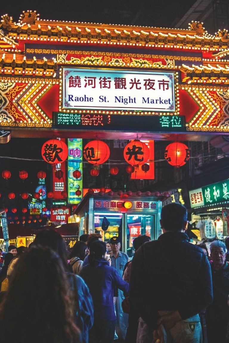 Things to do in Taiwan: Crowds walking under the illuminated entrance sign for Raohe Street Night Market in Taipei, surrounded by glowing lanterns and neon lights at night.