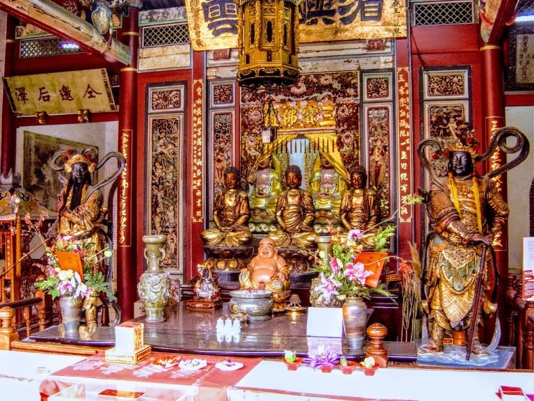 Ornate Buddhist temple altar in Taiwan with golden statues, carved wooden panels, offerings, and red columns.