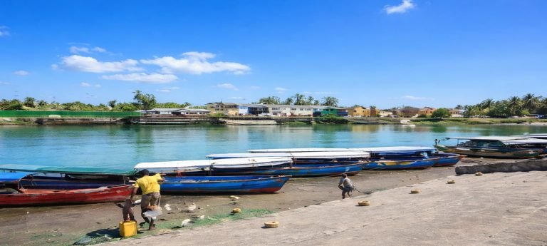 Fishing boats lined along the waterfront in Tamatave (Toamasina), Madagascar, with fishermen preparing nets under a bright blue sky.